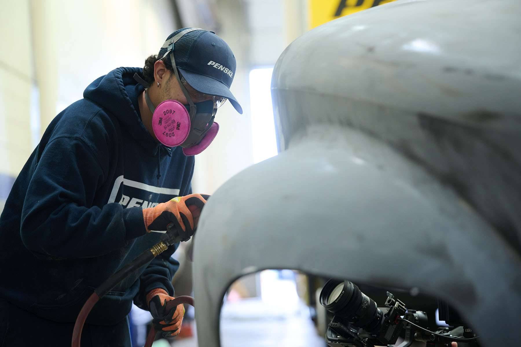 A person sands the front of a semi-truck cab.