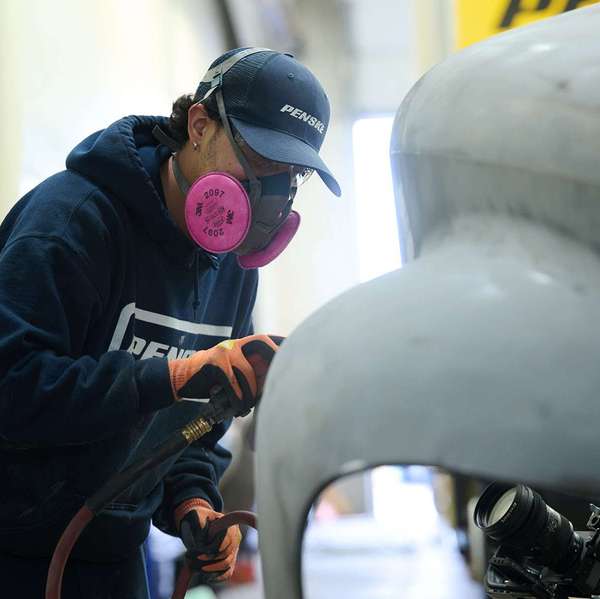 A person sands the front of a semi-truck cab.