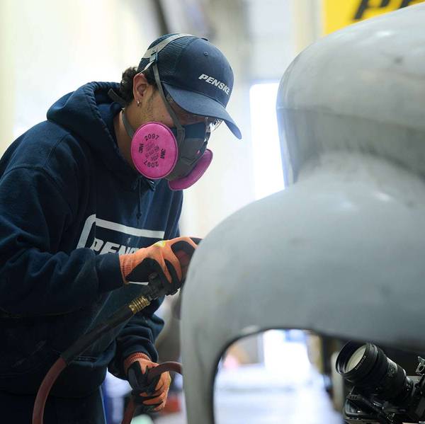 A person sands the front of a semi-truck cab.