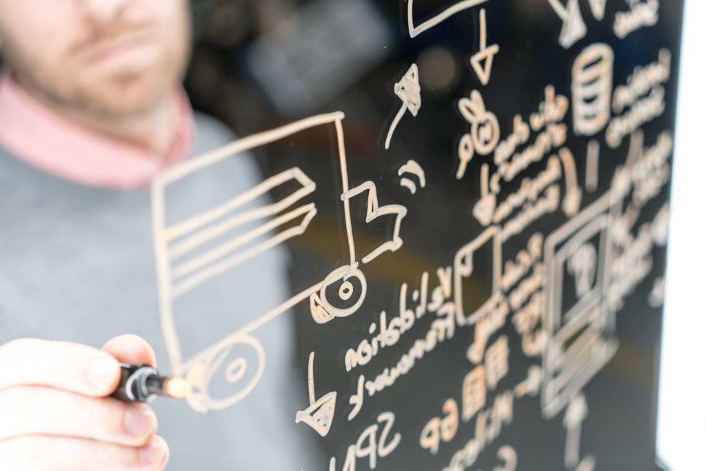 A person uses a marker to draw on a clear whiteboard.