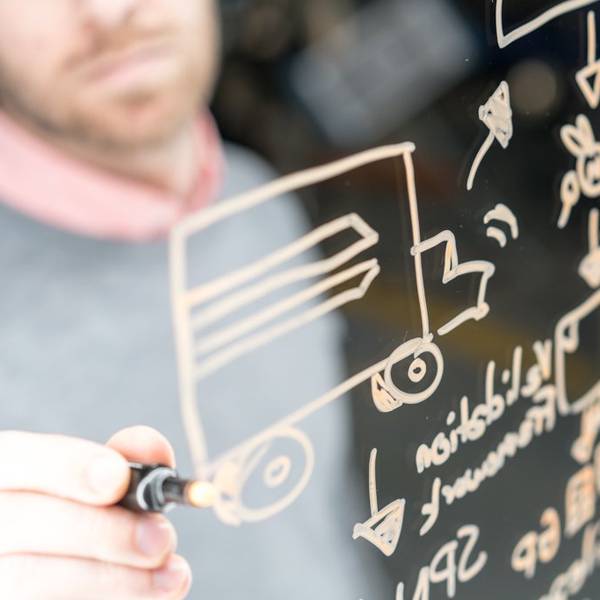 A person uses a marker to draw on a clear whiteboard.