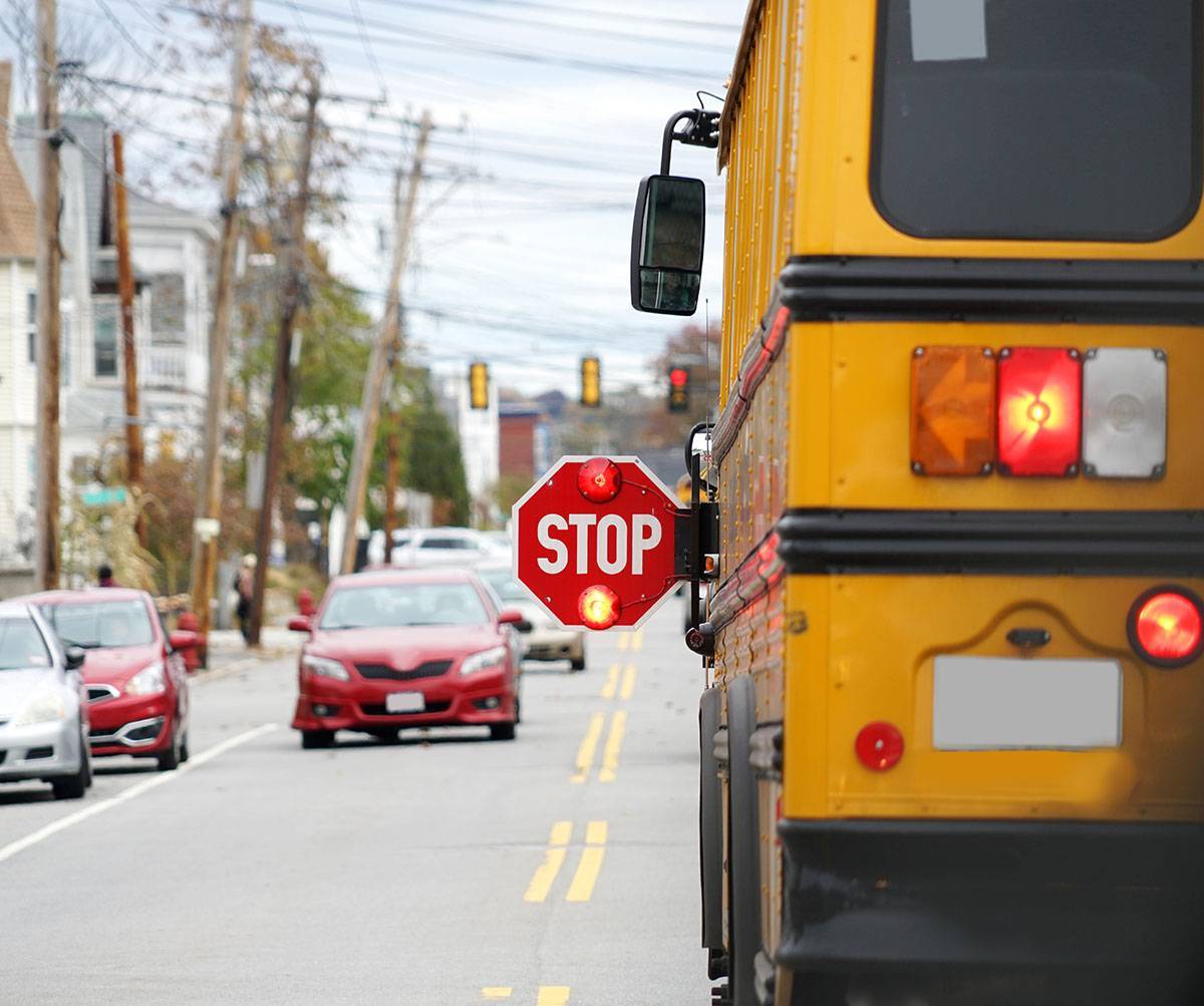 A school bus stopped on the road with it's stop sign out and flashing.