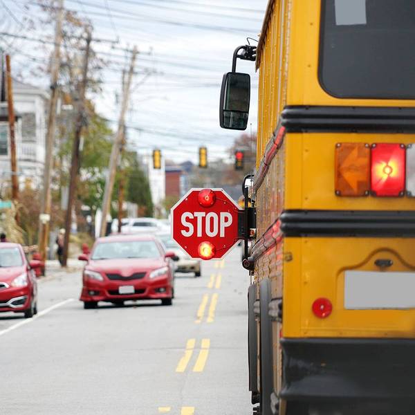 A school bus stopped on the road with it's stop sign out and flashing.