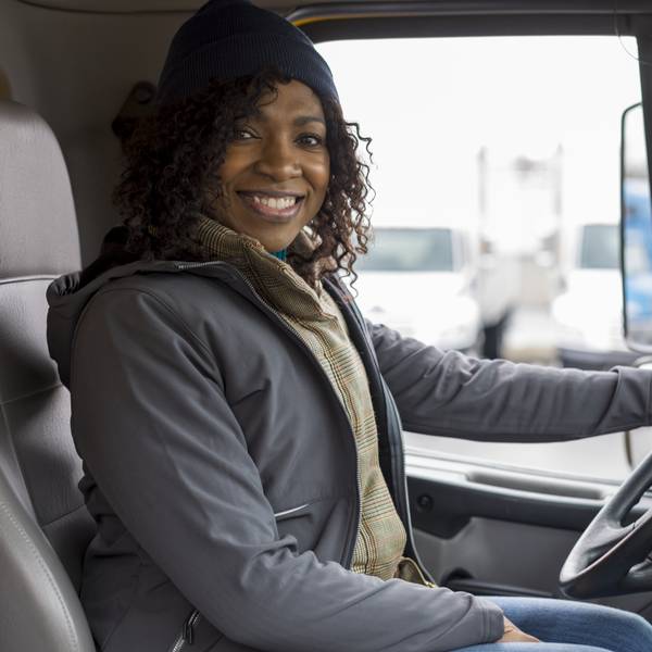 A smiling female driver sits behind the wheel of a truck.
