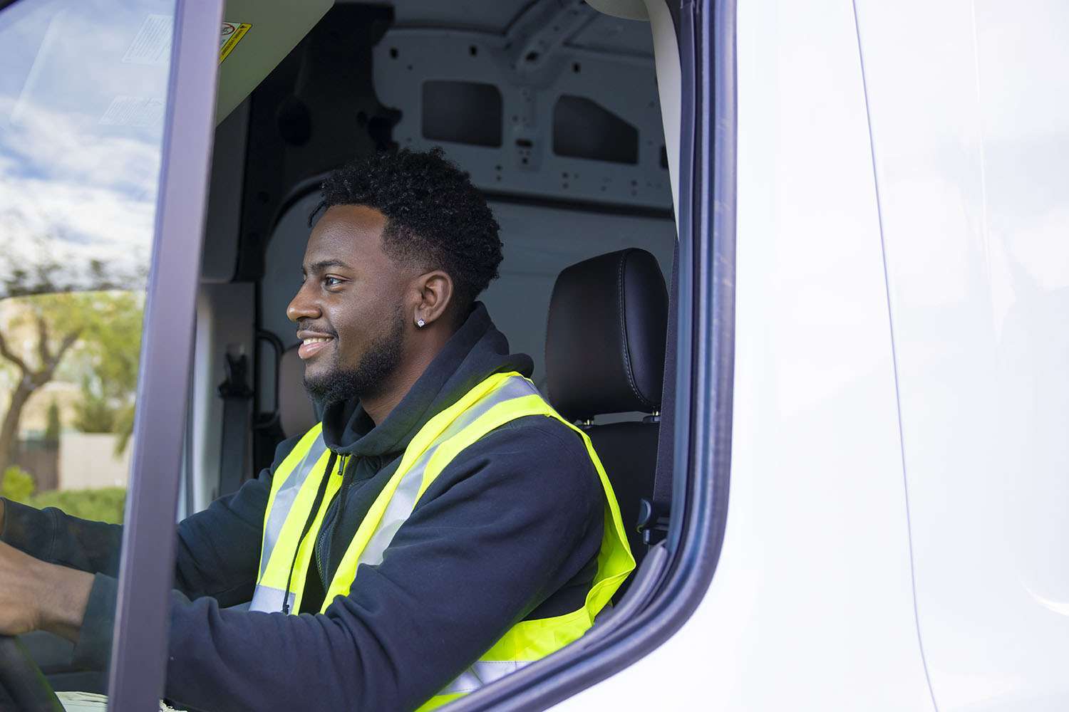 A smiling truck driver sits in the cab of a white truck.