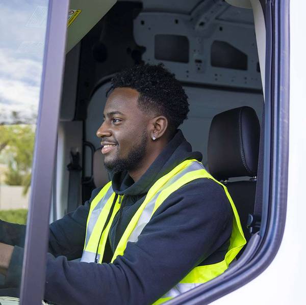 A smiling truck driver sits in the cab of a white truck.