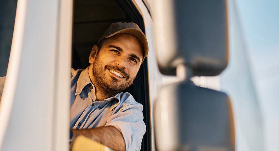 A smiling truck drivers looks out his driver-side truck window.