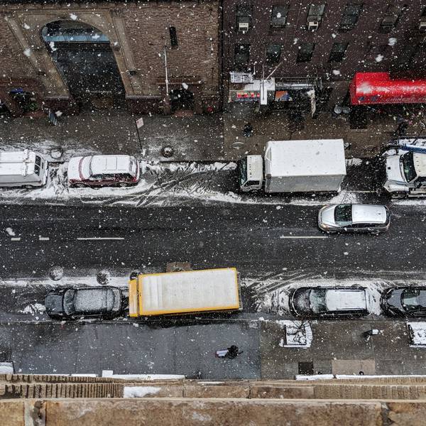 A snowy city street from above, crowded with cars and trucks.