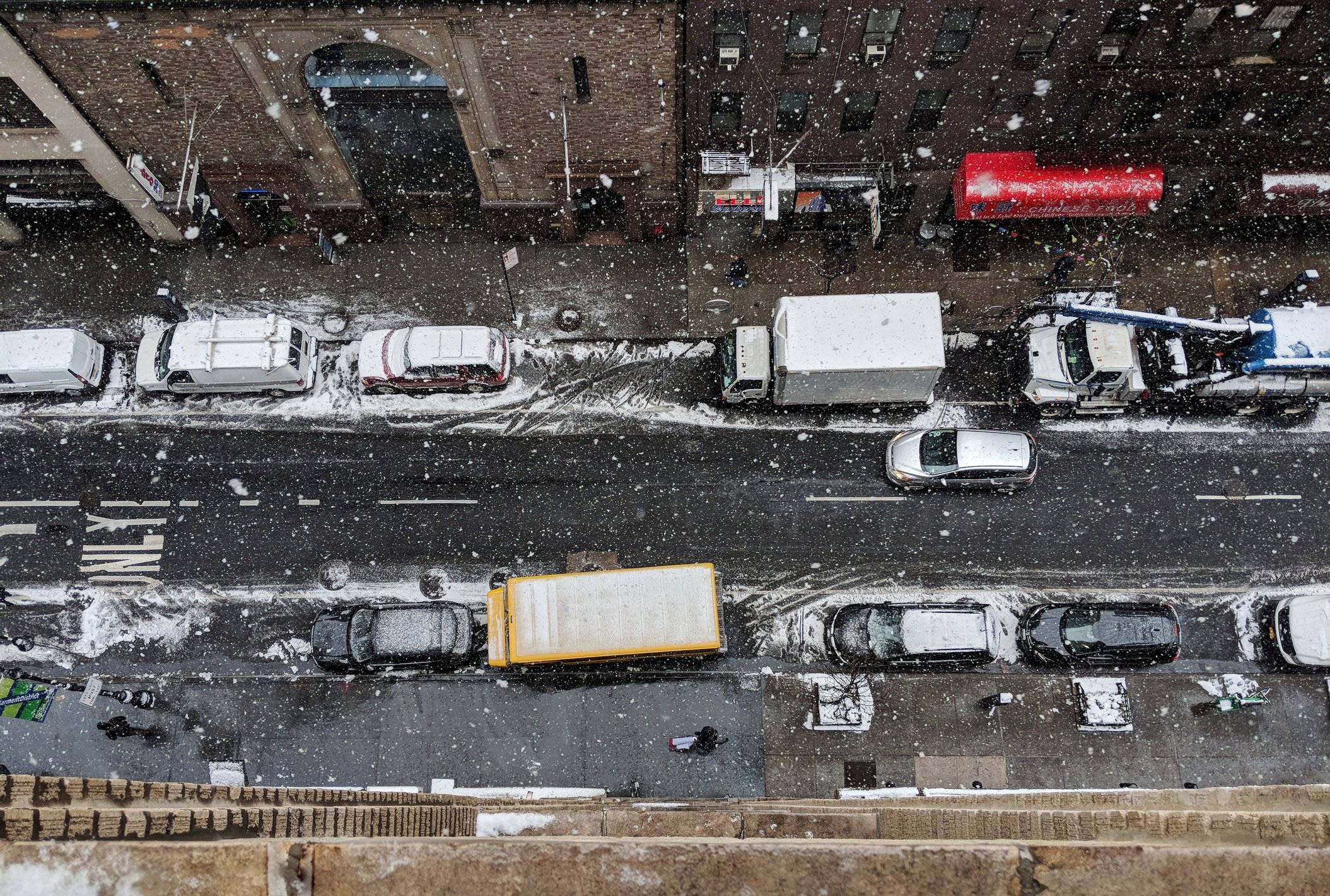 A snowy city street from above, crowded with cars and trucks.