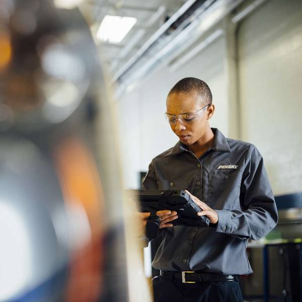 A technician looks at a handheld digital device while working on a semi-truck.