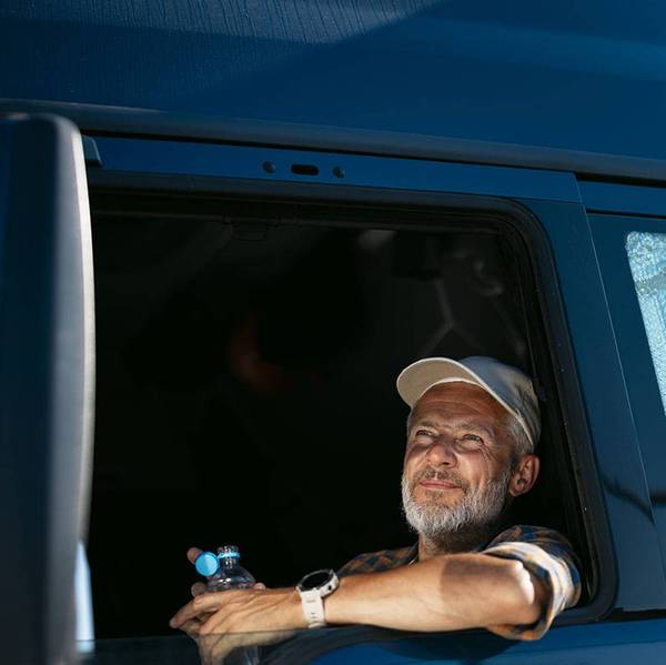A truck driver in a truck cab window holding an open bottle of water.