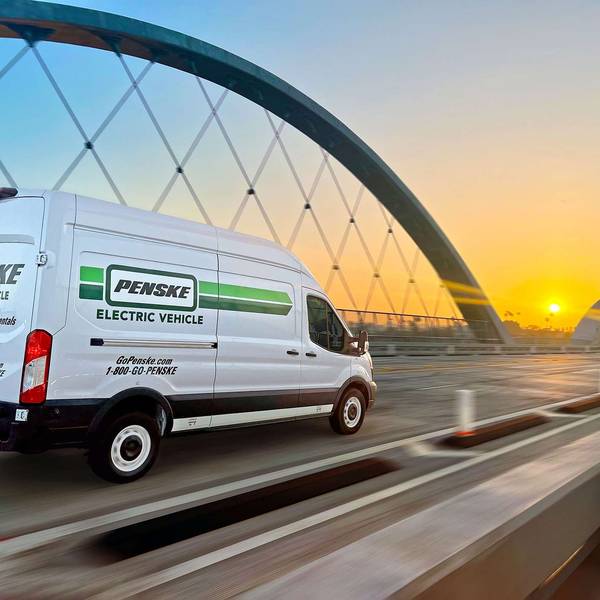 A white and green Penske electric cargo van drives over a bridge at sunset.