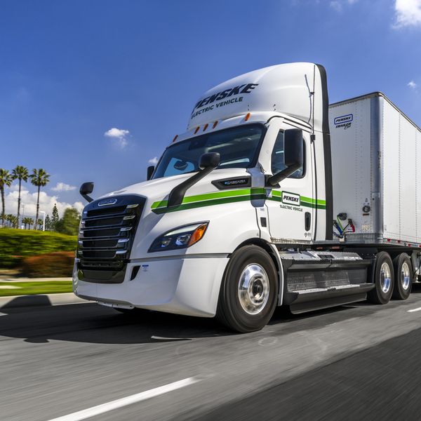 A white and green Penske Electric Truck drives on the road.