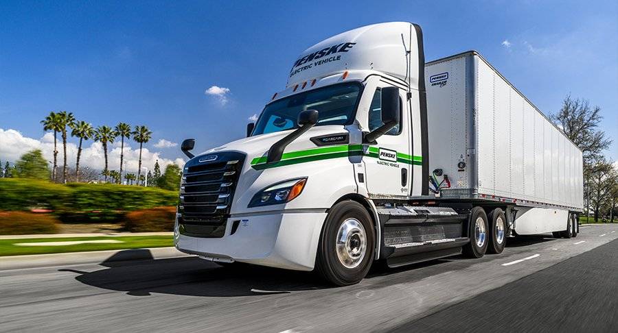 A white and green Penske Electric Truck drives on the road.