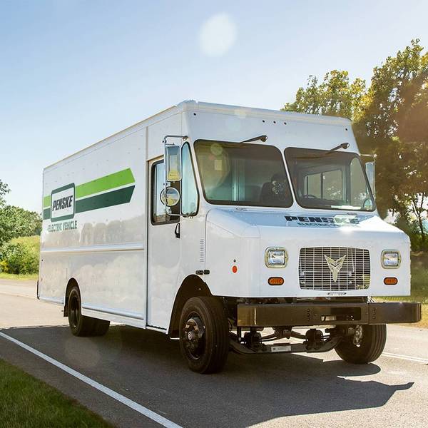 A white electric Penske step-van drives up the road on a sunny day.
