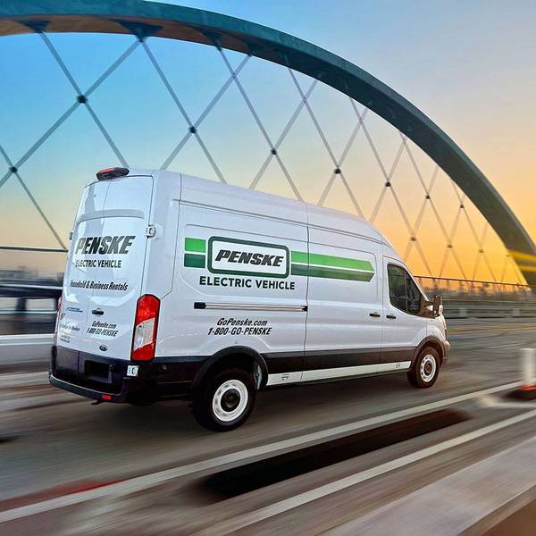 A white Penske electric cargo van drives on a freeway bridge at sunset.