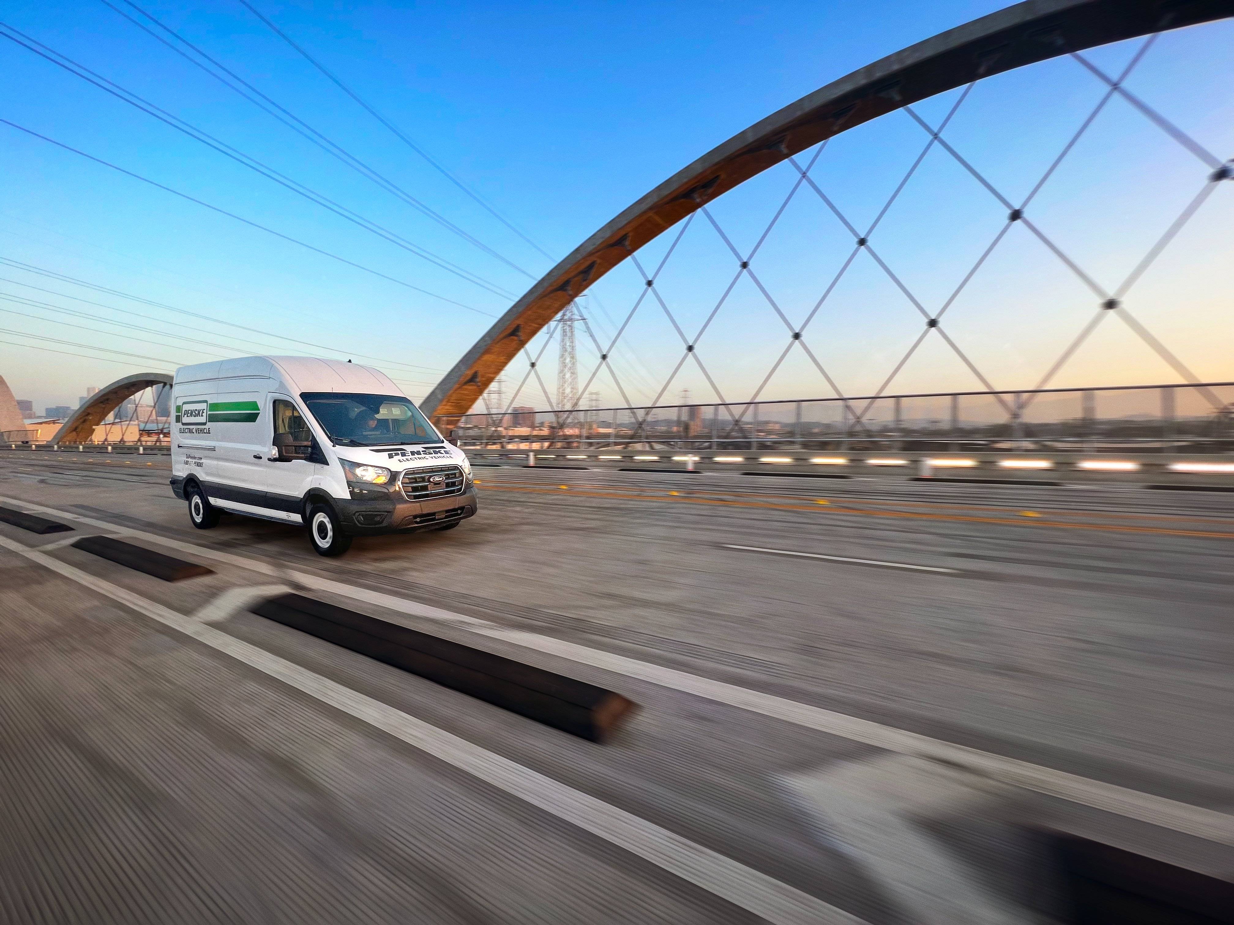 A white Penske electric cargo van drives over a bridge.