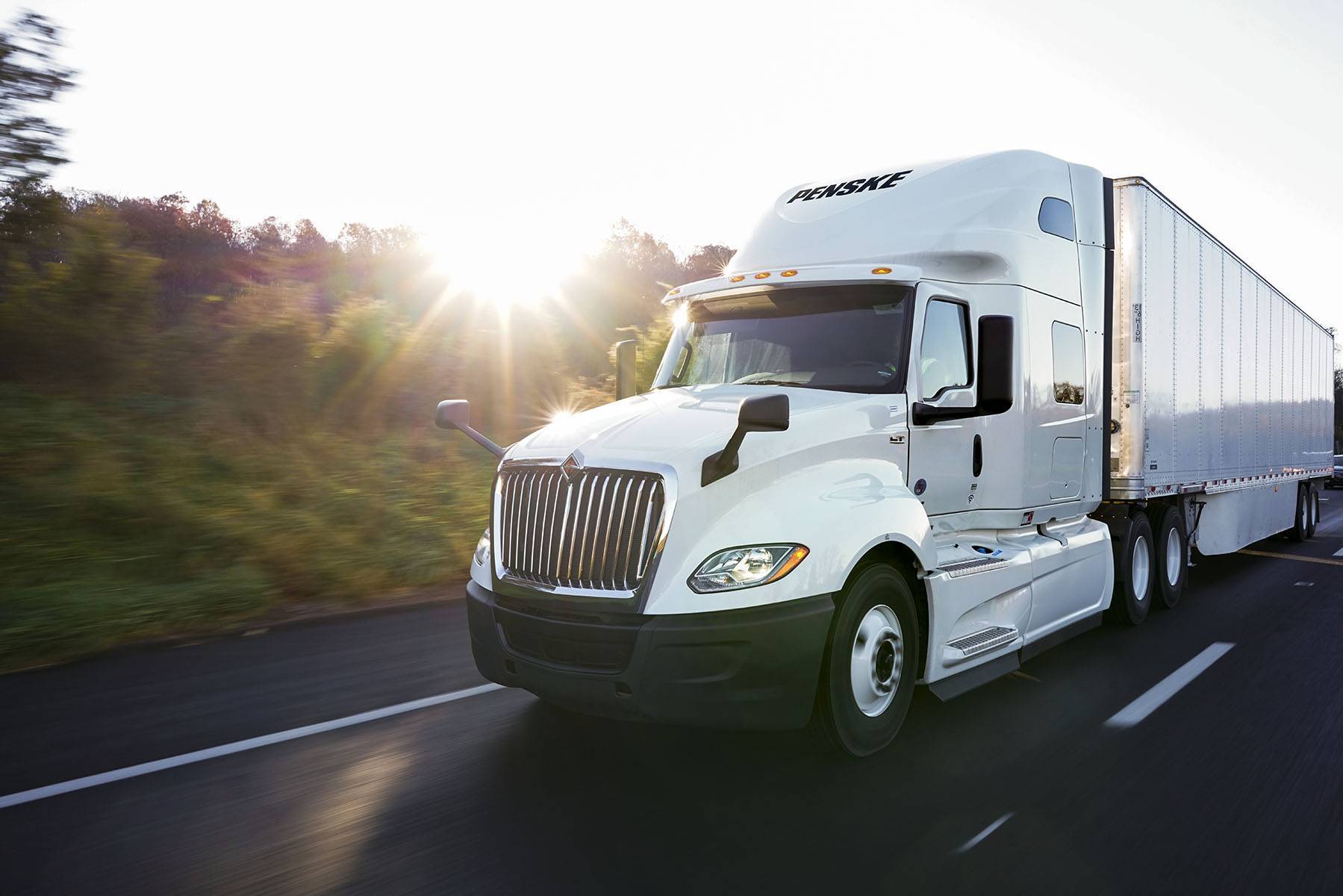 A white Penske semi-truck and trailer drive on a highway.