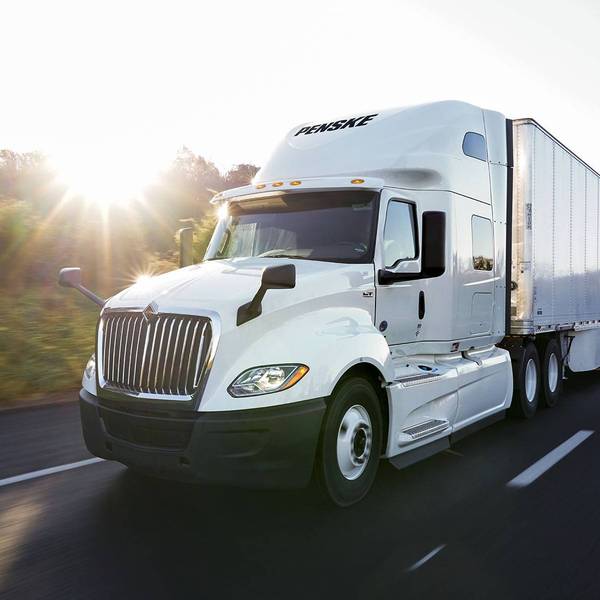 A white Penske semi-truck and trailer drive on a highway.
