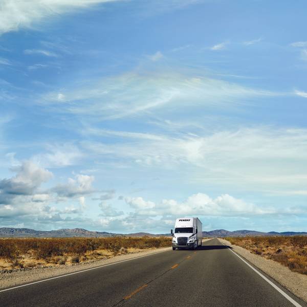 A white Penske semi-truck drives on an open desert road.