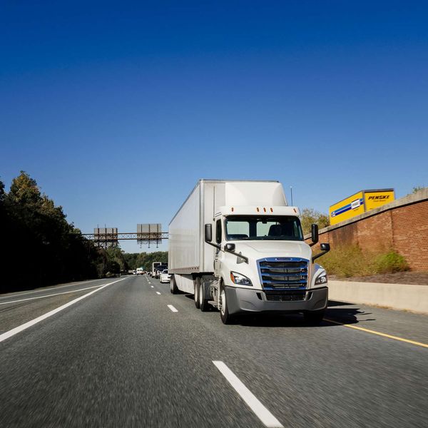 A white Penske semi-truck drives one way on a freeway past a yellow Penske box truck going the other way.