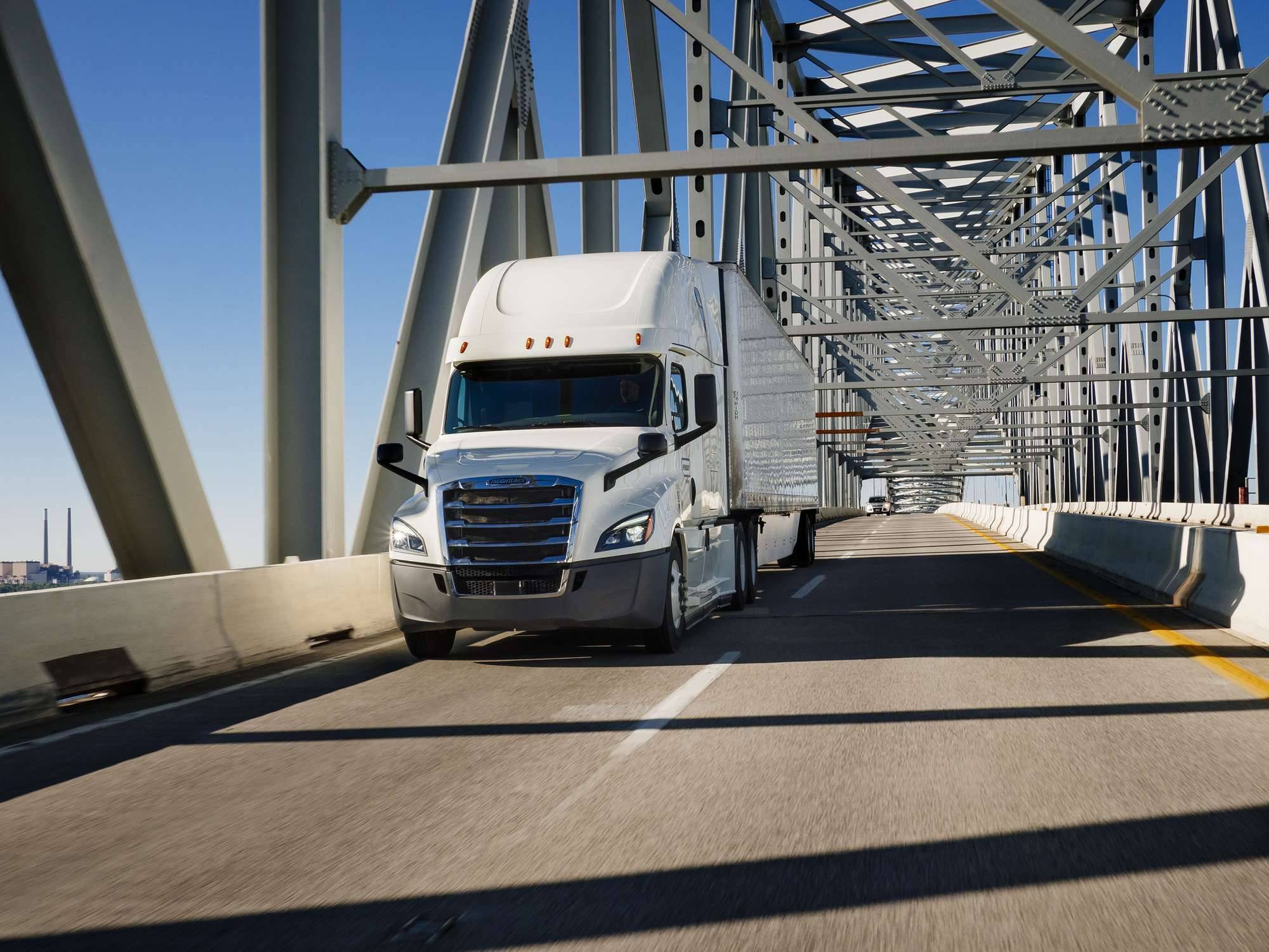A white Penske semi-truck drives over a bridge.