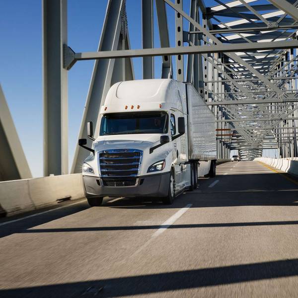 A white Penske semi-truck drives over a bridge.
