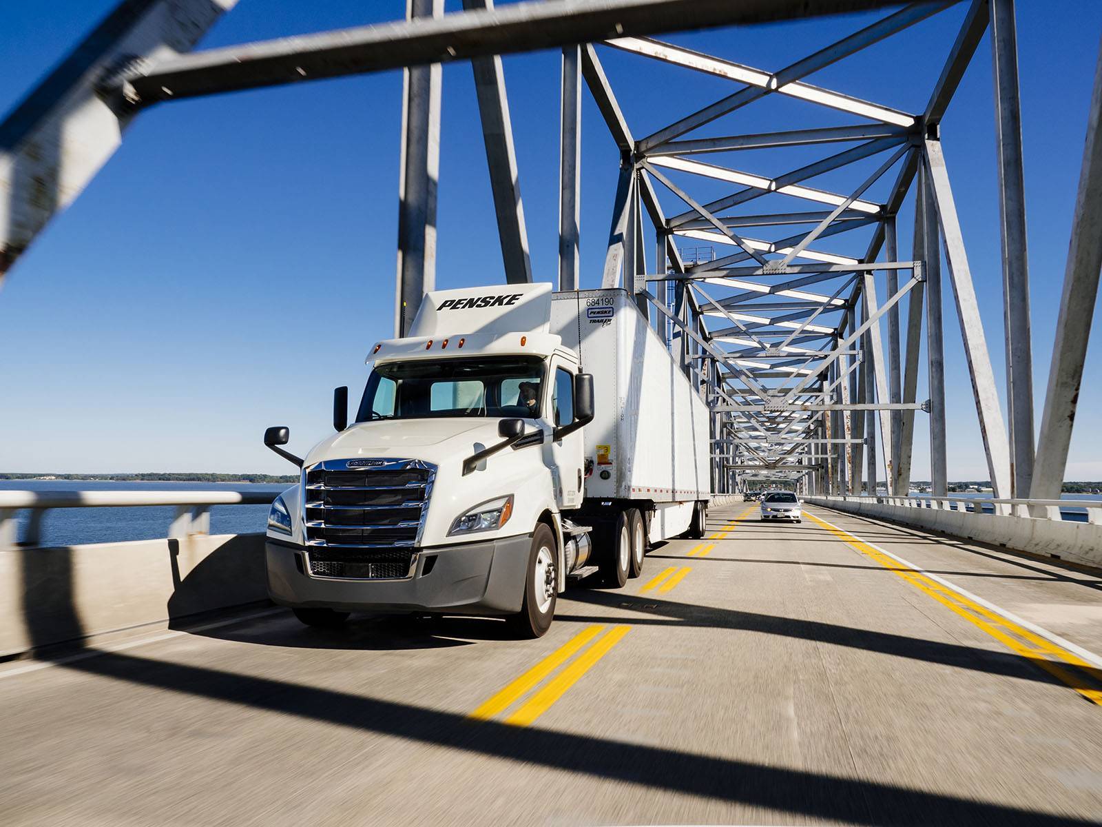 A white Penske semi-truck drives over a bridge.