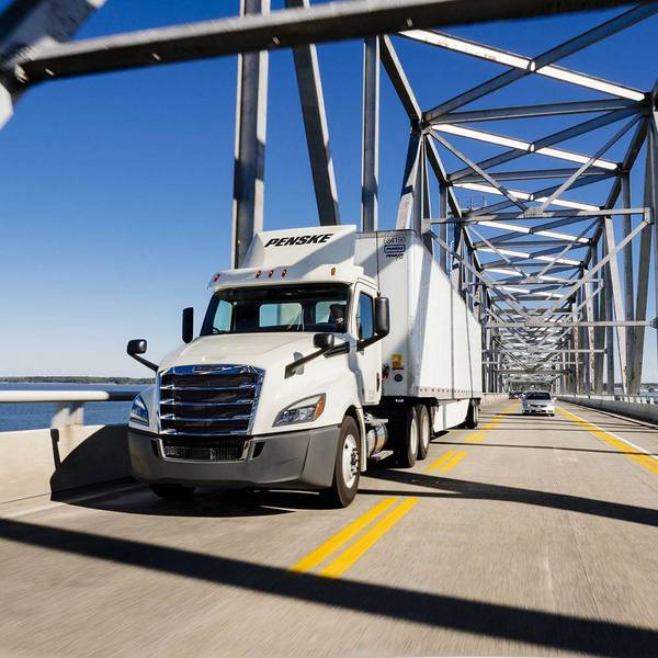 A white Penske semi-truck drives over a bridge.