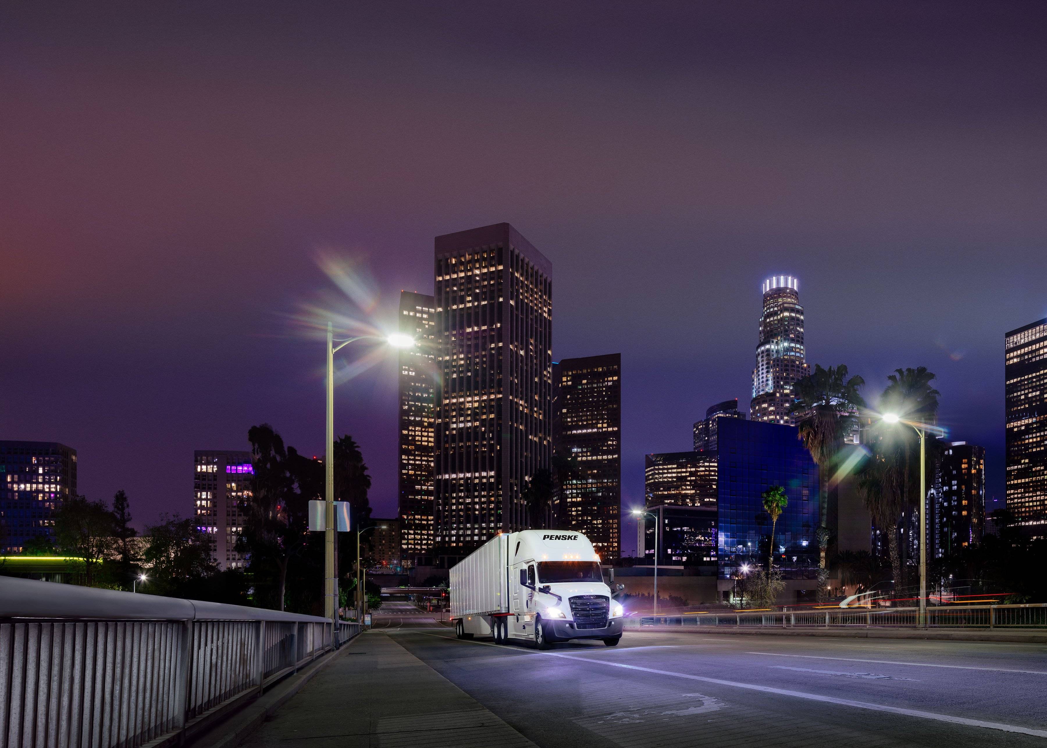 A white Penske semi-truck drives through a city at night.