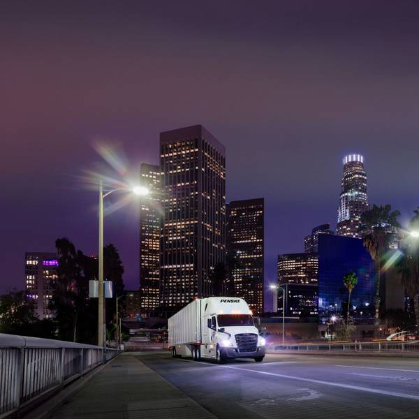 A white Penske semi-truck drives through a city at night.