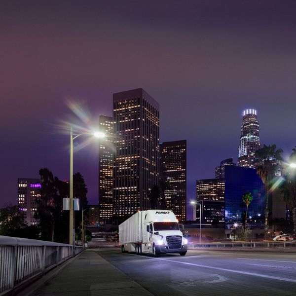 A white Penske semi-truck drives through a city at night.