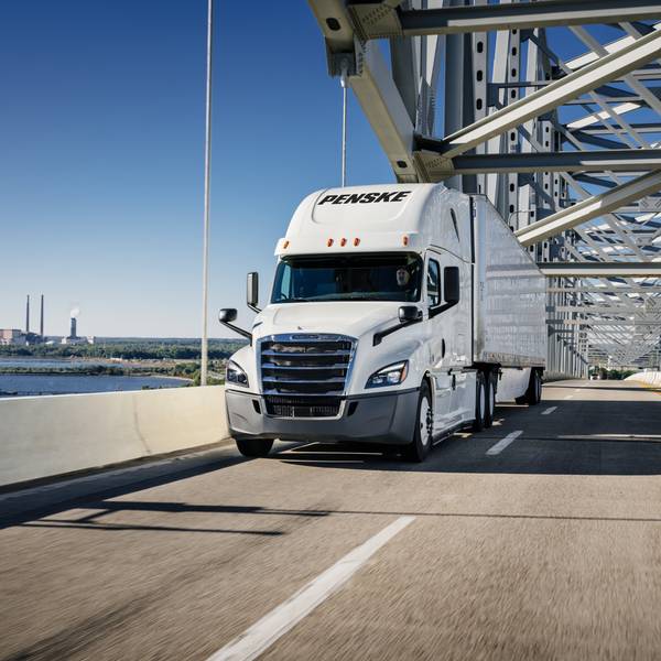 A white Penske tractor and trailer drives on a bridge.