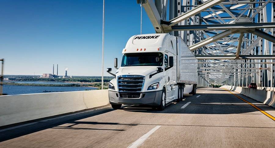 A white Penske tractor and trailer drives on a bridge.
