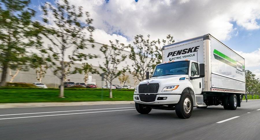 A white Penske truck drives on the road.