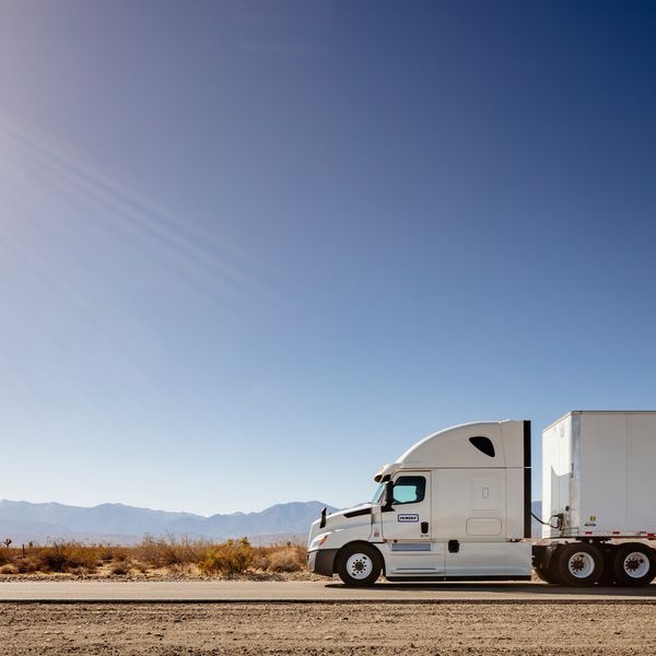 A white Penske truck driving on a desert road.