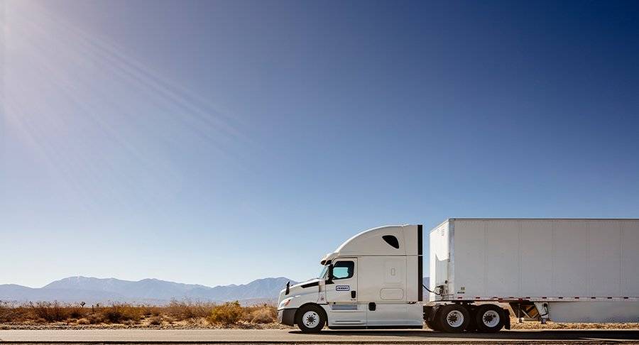 A white Penske truck driving on a desert road.