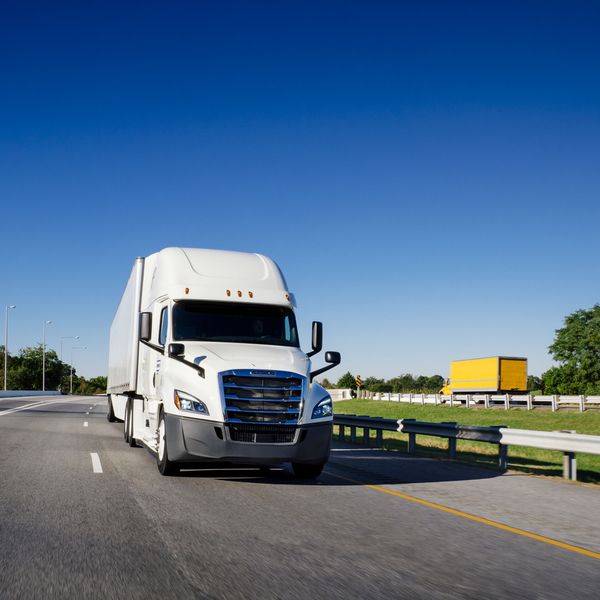 A white semi-truck and yellow box truck drive on opposite sides of the highway.