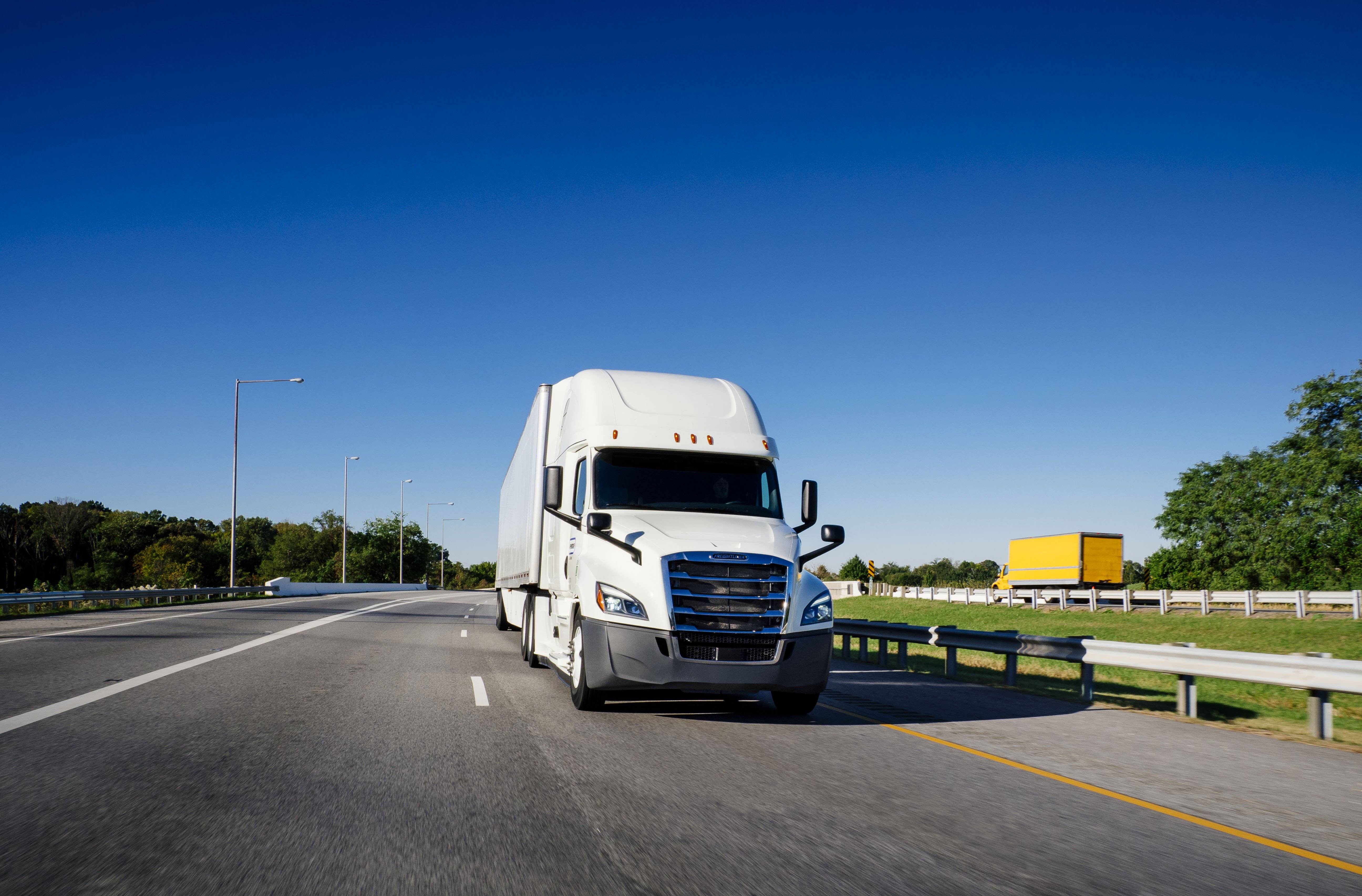 A white semi-truck and yellow box truck drive on opposite sides of the highway.