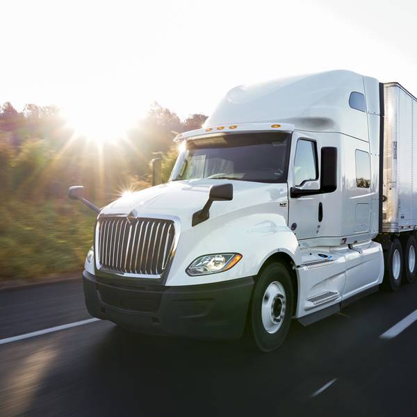 A white semi-truck drives down the road at sunset.