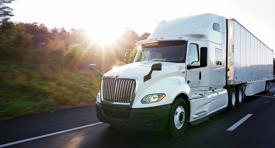 A white semi-truck drives down the road at sunset.