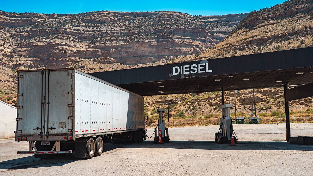 A white semi-truck fueling up under a black Diesel sign with mountains in the background.