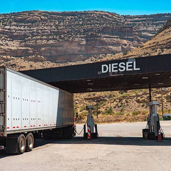A white semi-truck fueling up under a black Diesel sign with mountains in the background.