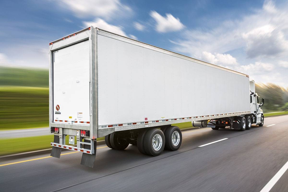 A white semi-truck with attached white semi-trailer driving down the road.