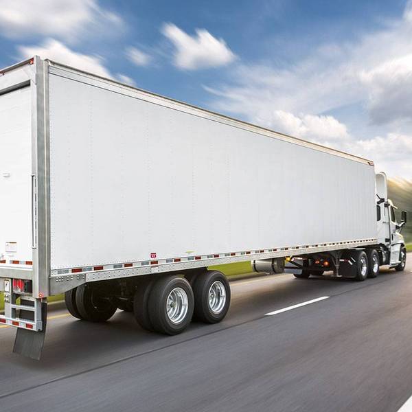 A white semi-truck with attached white semi-trailer driving down the road.