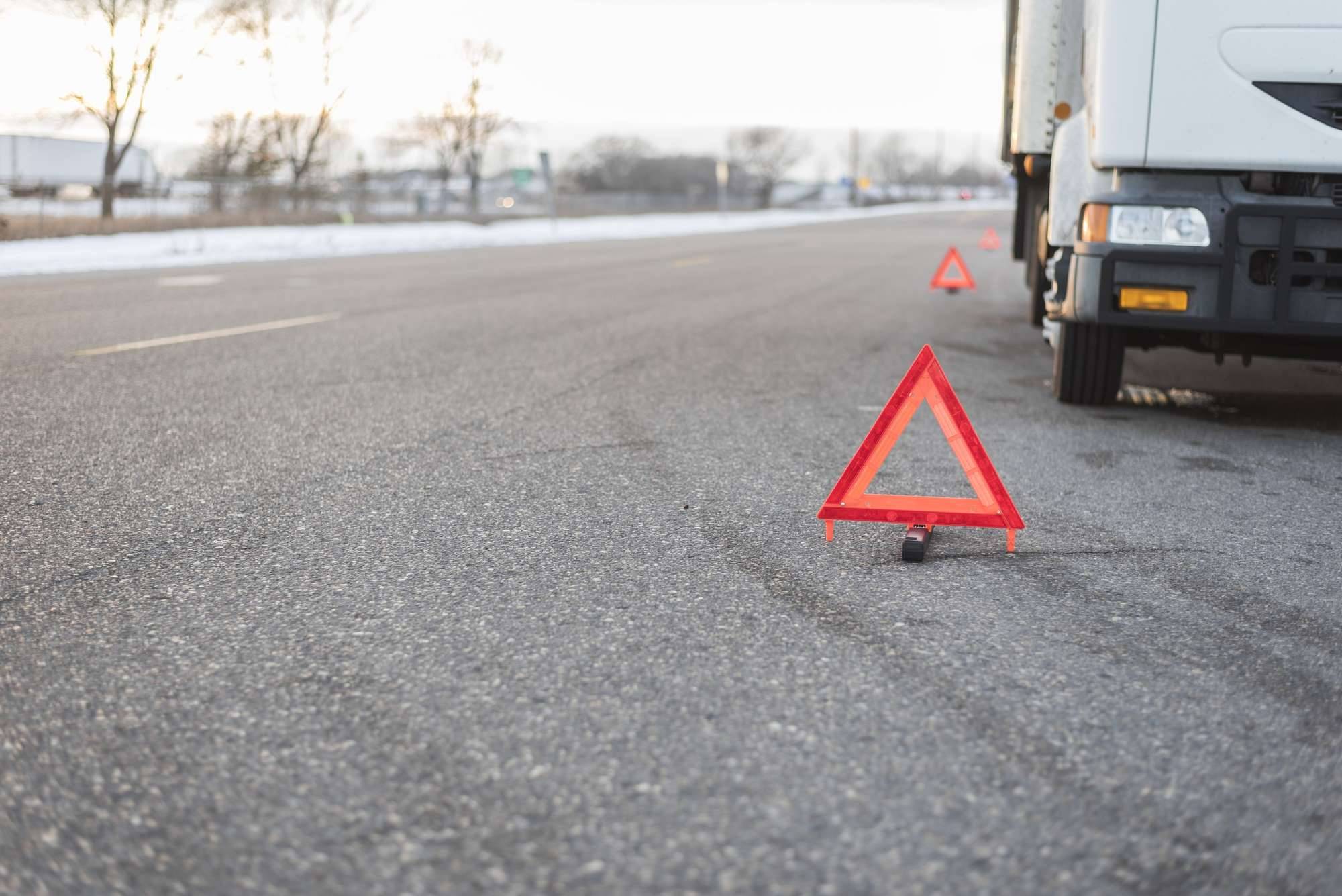 A white truck broken down on the side of the road surrounded by caution triangles.