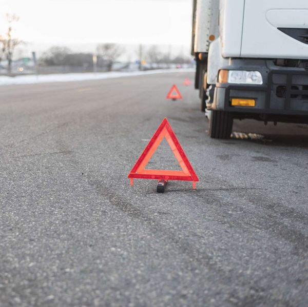 A white truck broken down on the side of the road surrounded by caution triangles.