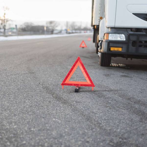 A white truck broken down on the side of the road surrounded by caution triangles.