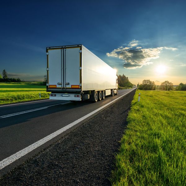 A white truck driving down a road in summer.