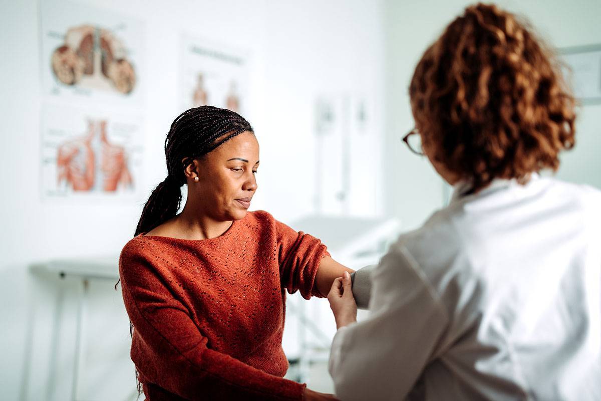 A woman in a red sweater has her blood pressure checked by a female doctor.